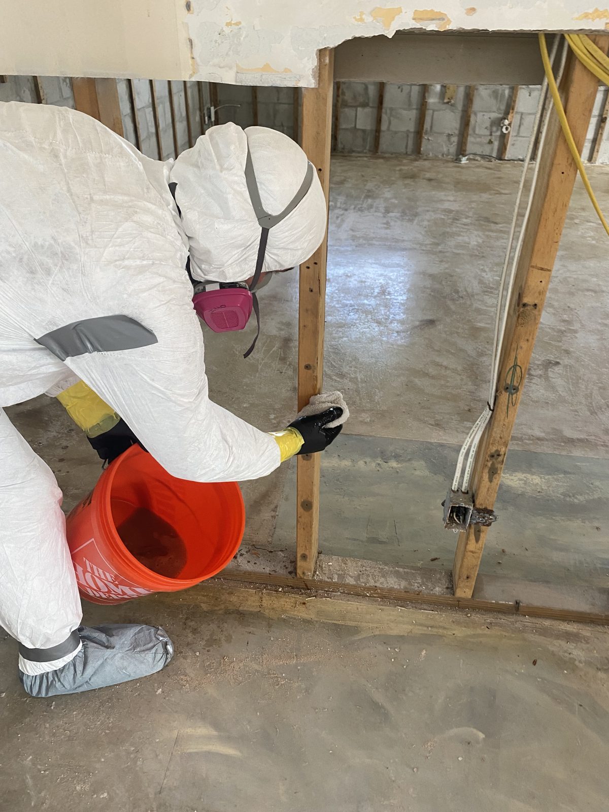 AIM technician in full protective gear hand-cleaning wall studs during mold remediation